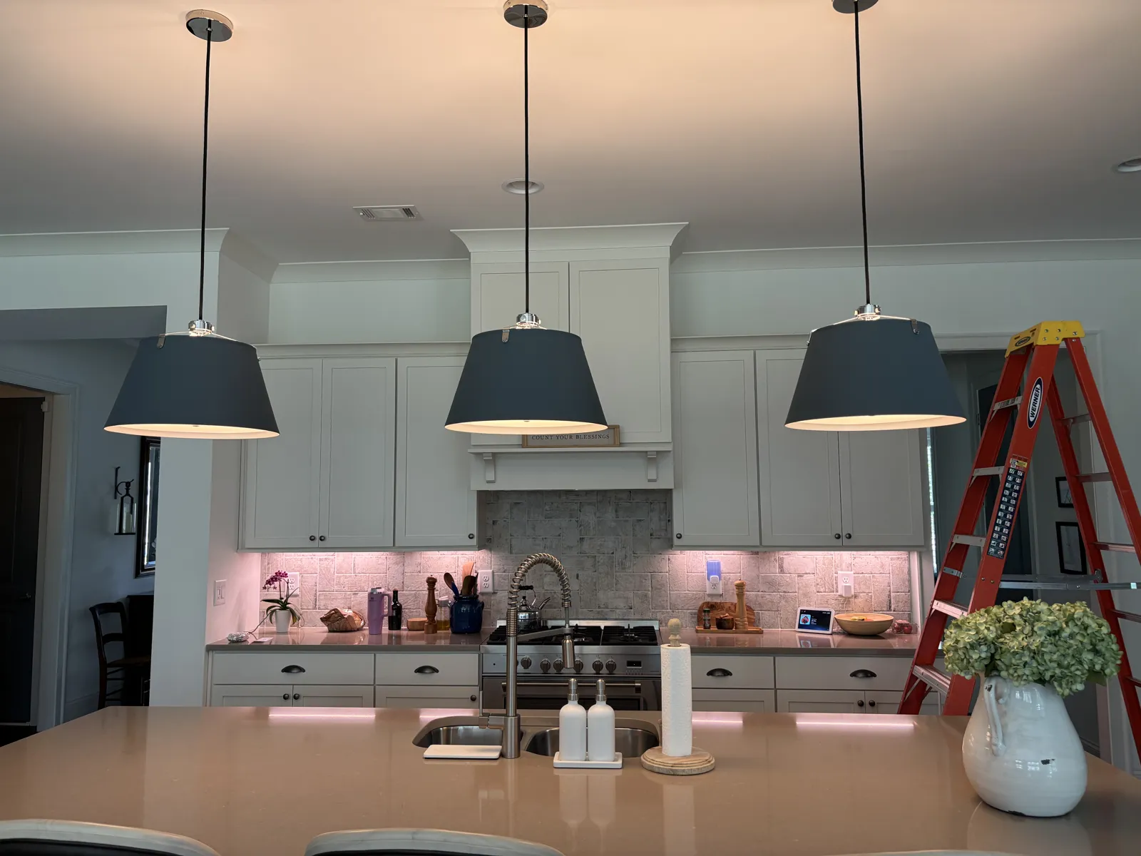 Three dark pendant lights installed over a kitchen island